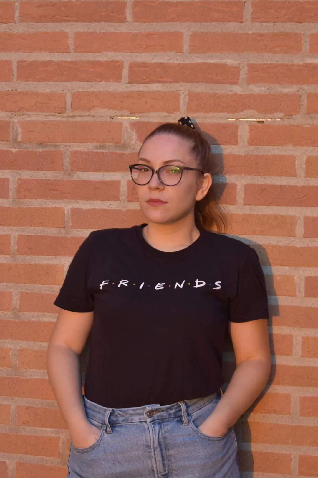 Maria in a black Friends t-shirt against a brick wall