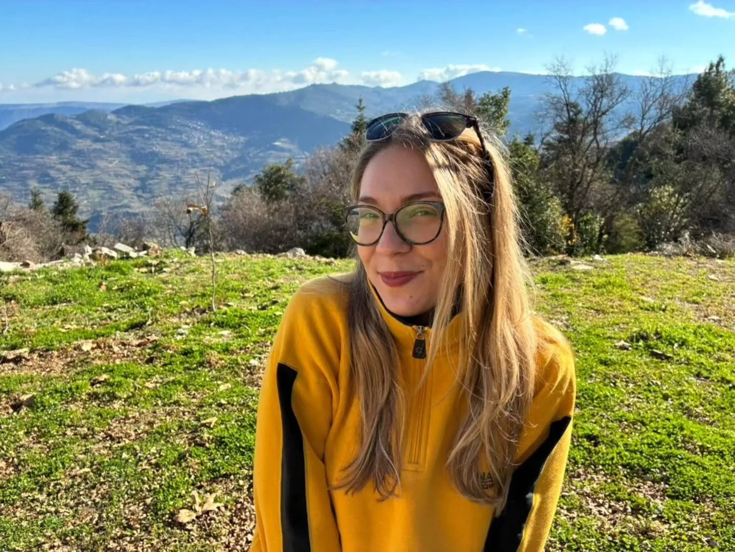 Maria in a yellow sweater on a hillside with mountains behind her