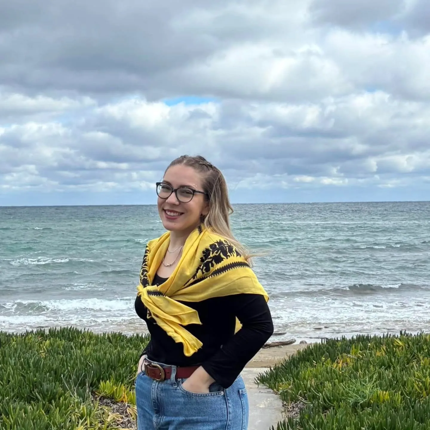 Maria on a beach with a yellow scarf under a cloudy sky