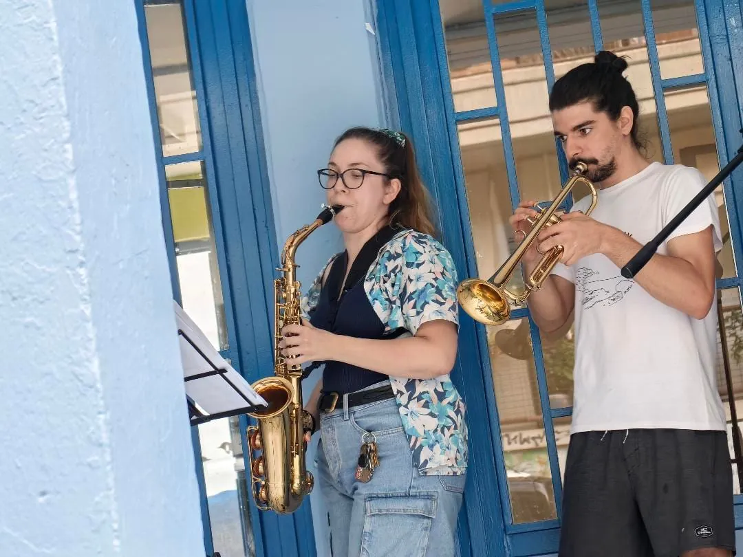 Maria on saxophone with a trumpeter, playing in the street