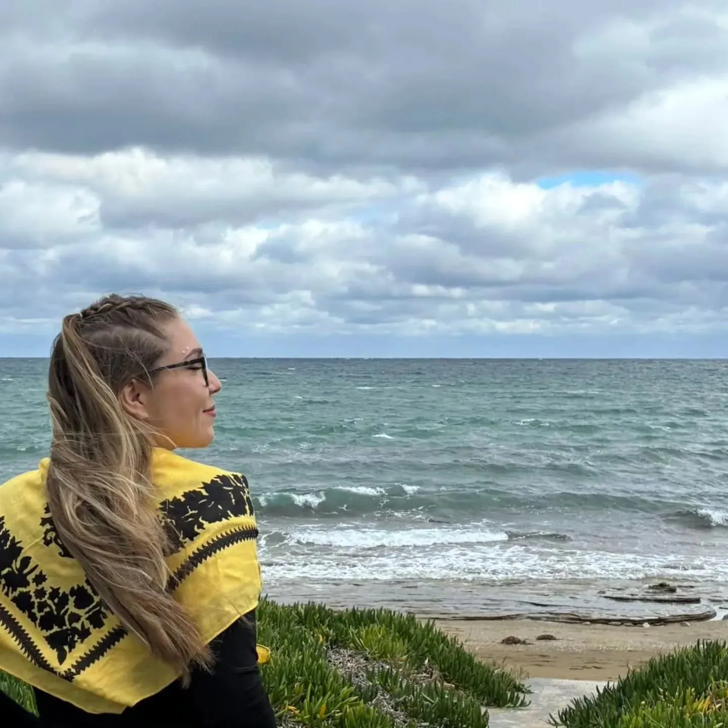 Maria on a beach with a yellow scarf, looking out to sea