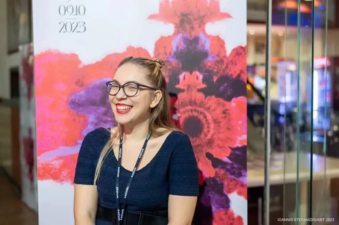 Maria laughing in front of the Athens International Film Festival wall, 2023