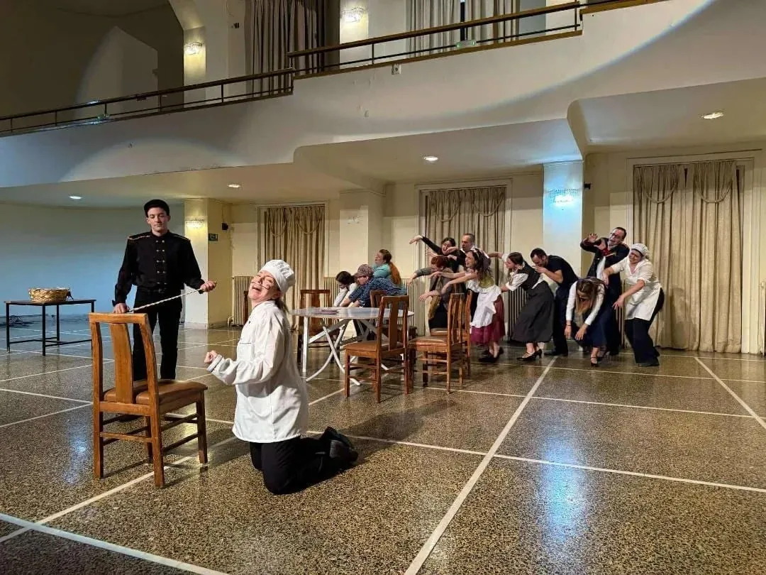 Rehearsal of Maroula's Fortune, Maria kneeling in a white costume among the cast