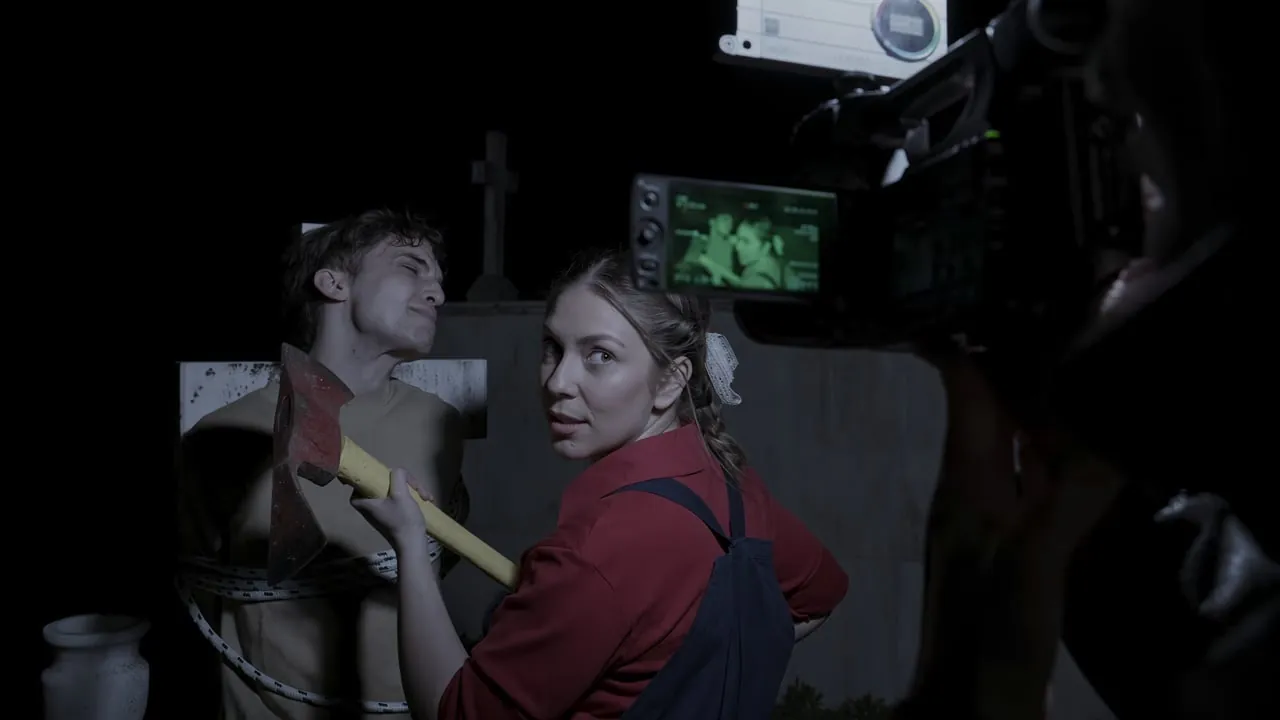 Behind the scenes of the Metronomos music video, Maria in a red shirt holding an axe in front of the camera