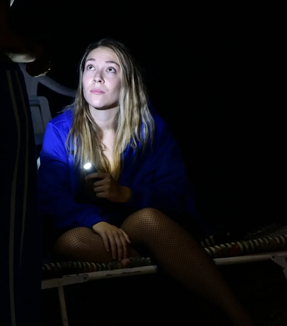 Maria on stage in blue light, holding a torch and looking up